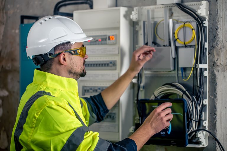 man-electrical-technician-working-switchboard-with-fuses-uses-tablet